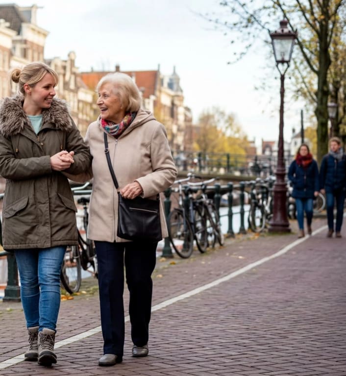 Helper en senior wandelen samen lachend langs een Amsterdamse gracht